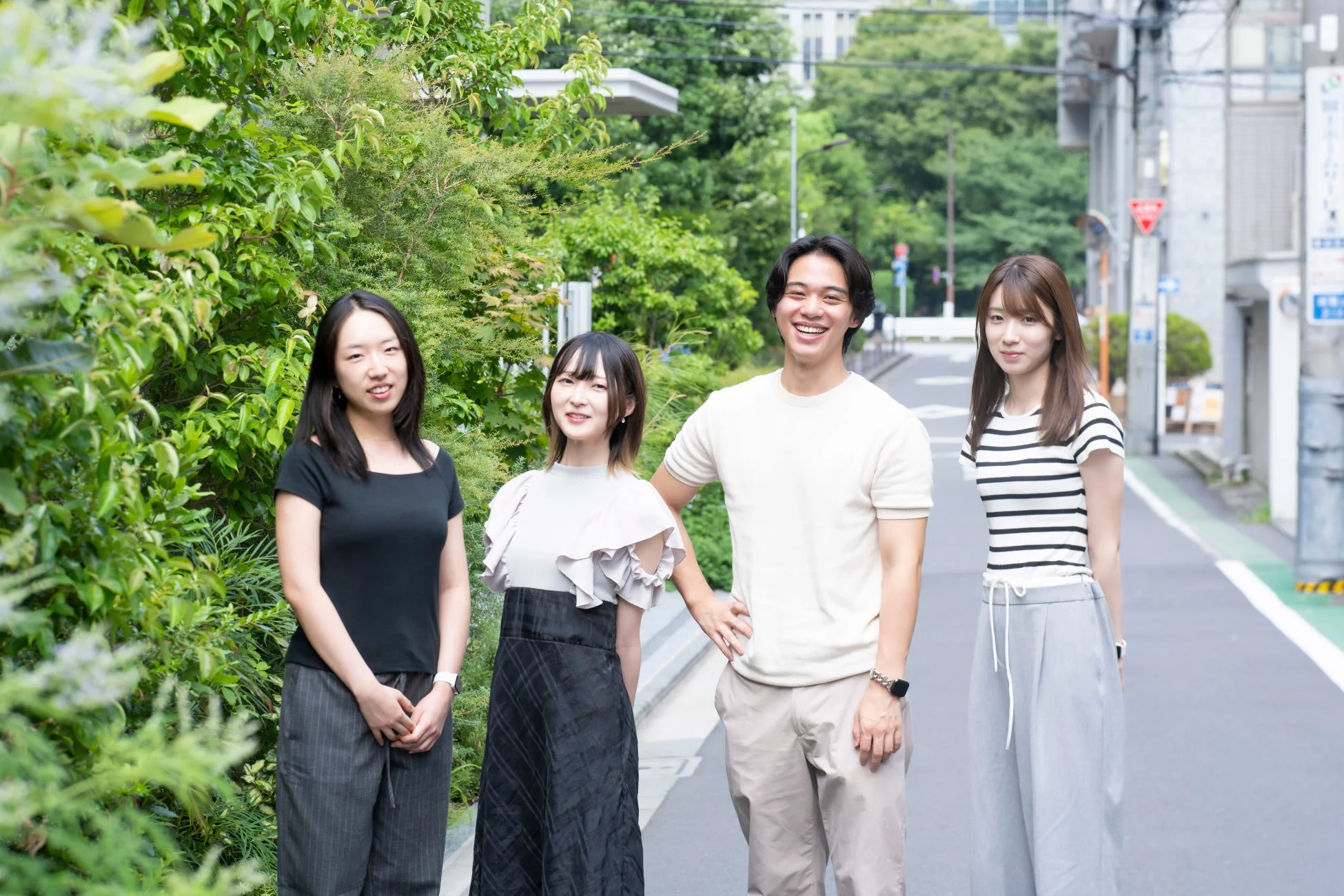 笑顔の男女4人がカジュアルな服装で並んで立っている