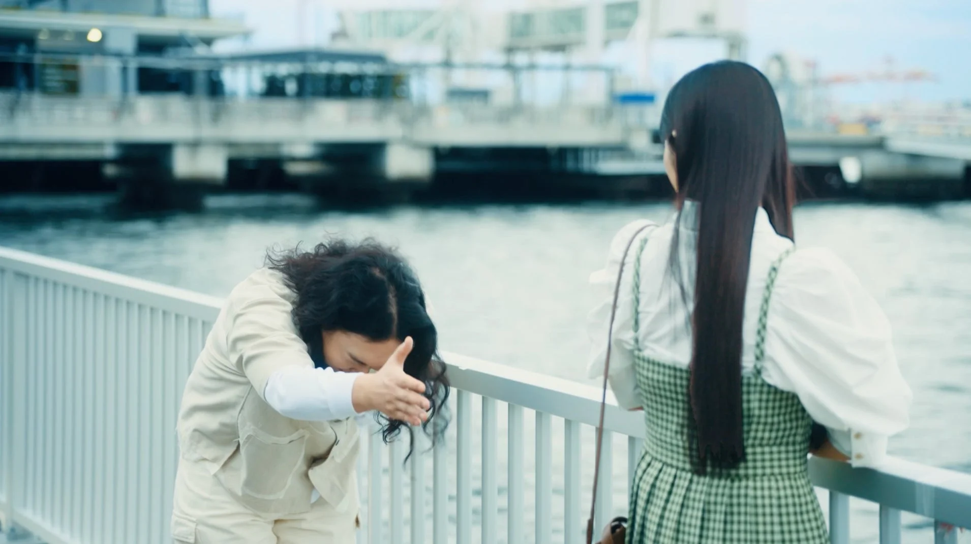 女性が顔を覆い、もう一人の女性が水面を見る