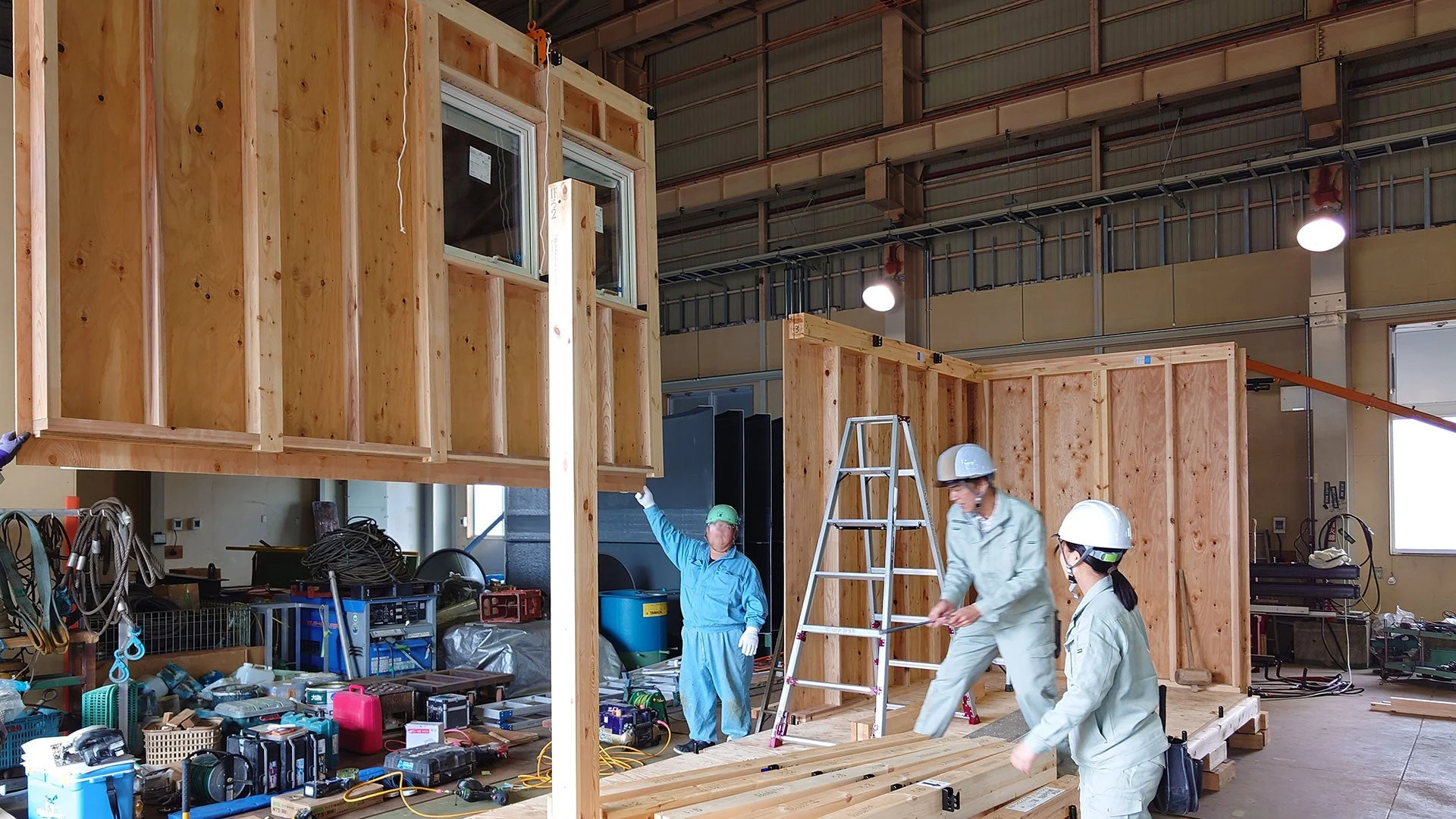 工場内で複数の作業員が木造建築のモジュールを組み立てている様子です。