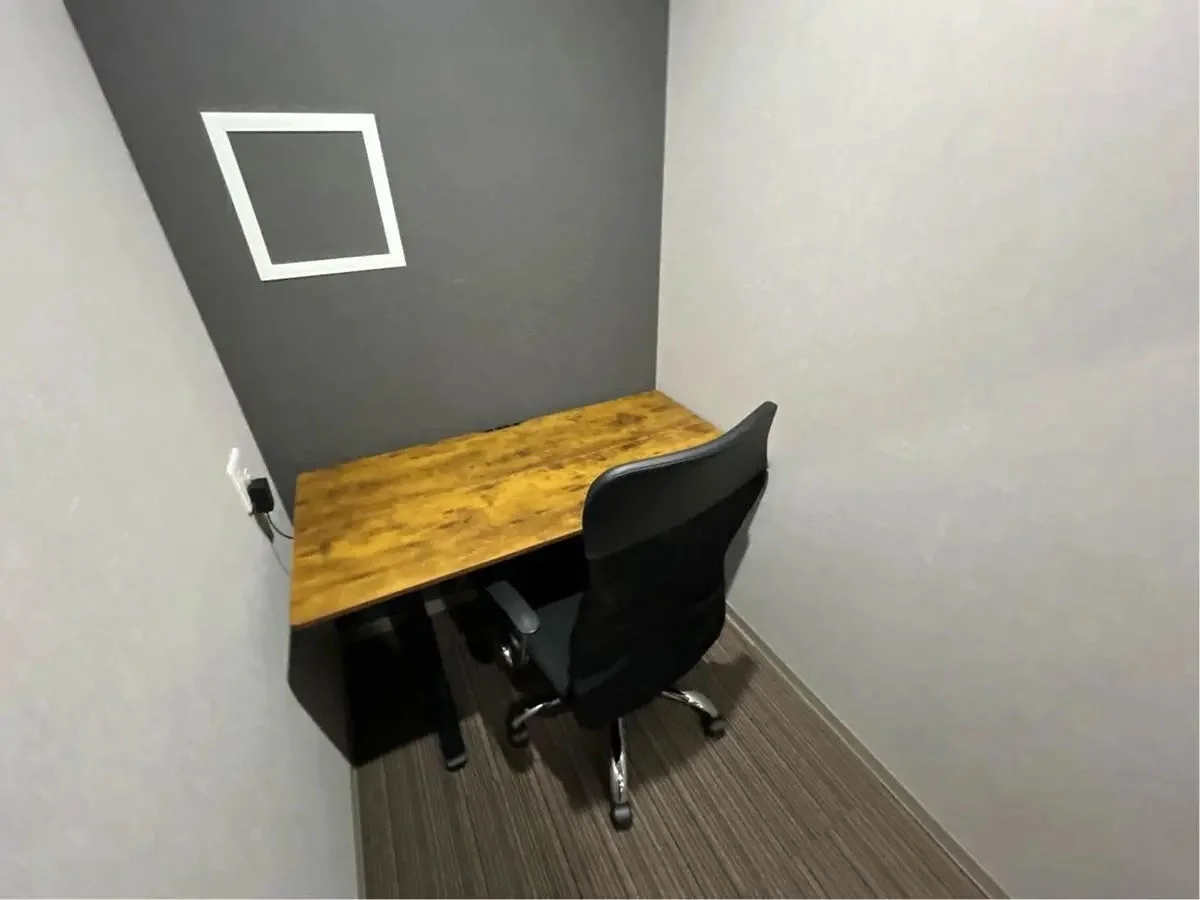 木目調のデスクと黒いオフィスチェアが置かれた、シンプルな個室ワークスペース