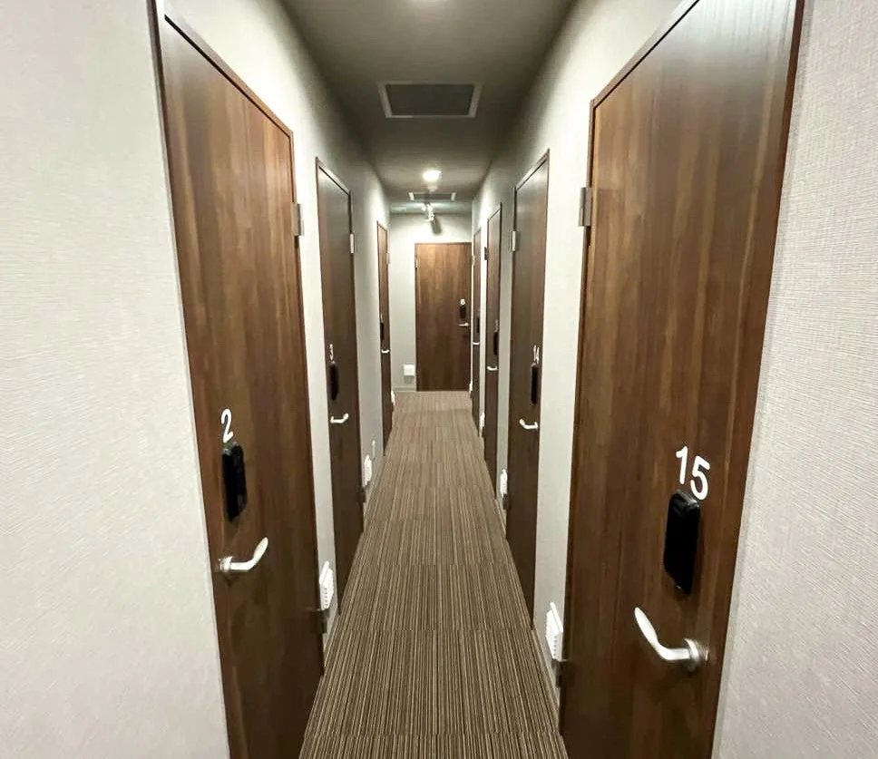薄暗い照明の細長い廊下で、両側に木目調のドアが並んでいます