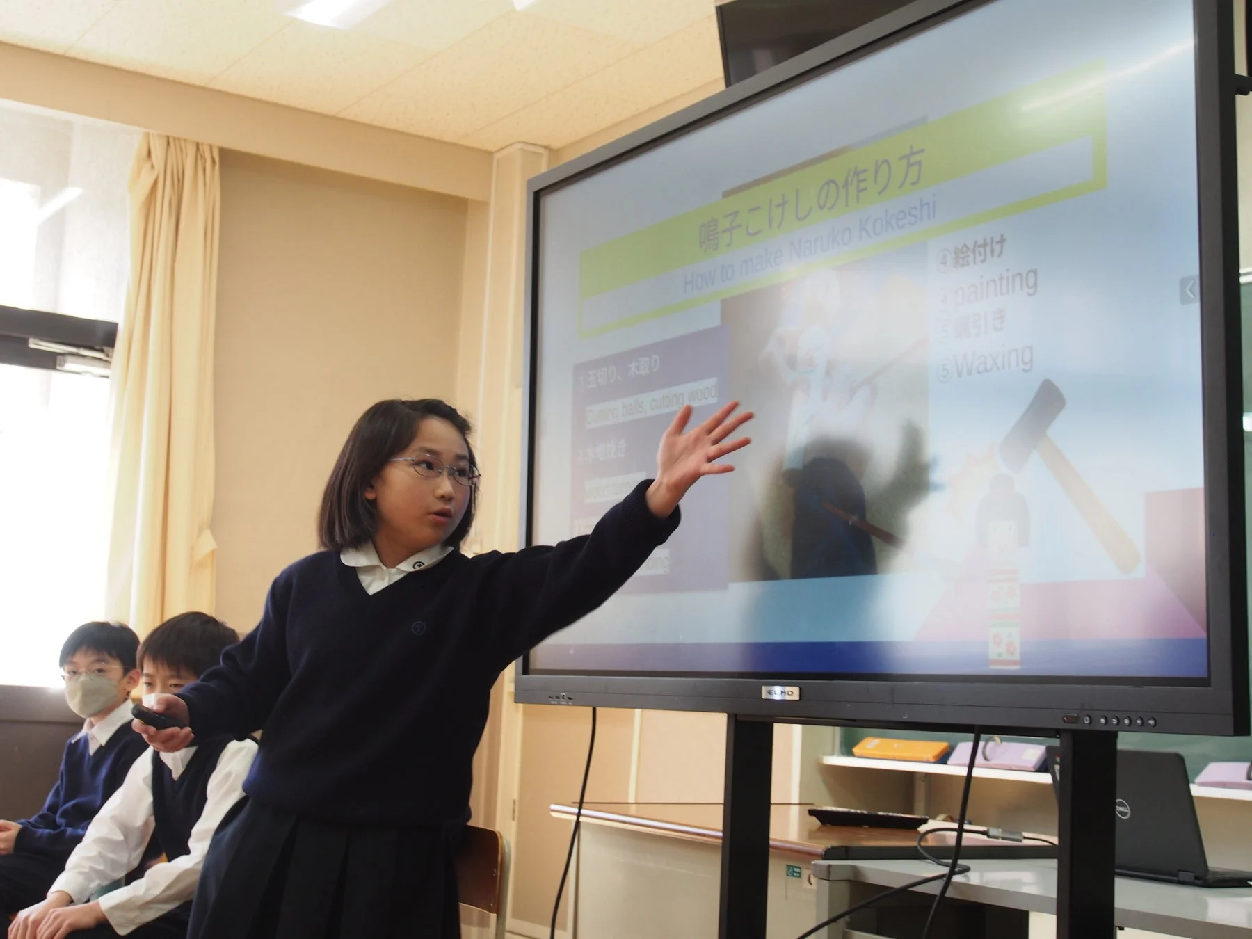 デジタルスクリーンで「鳴子こけしの作り方」をプレゼンする小学生