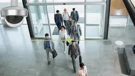 現代的な建物の入口を行き交うビジネスパーソンとセキュリティカメラ