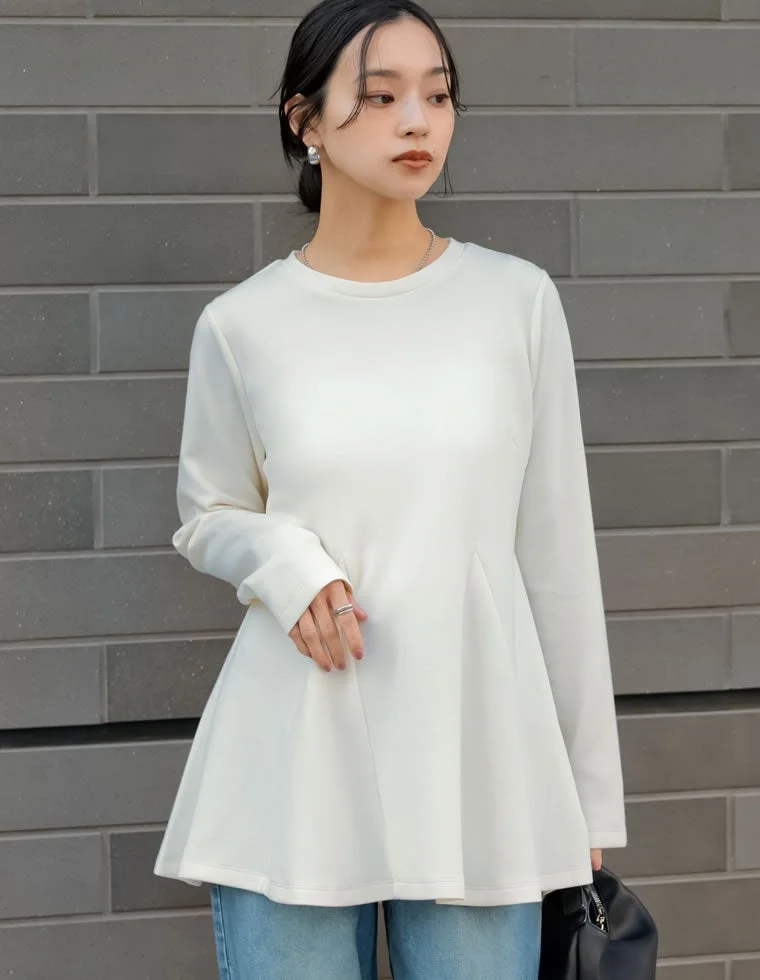 白い長袖のペプラムトップスとライトブルーのデニムを着用した若い女性