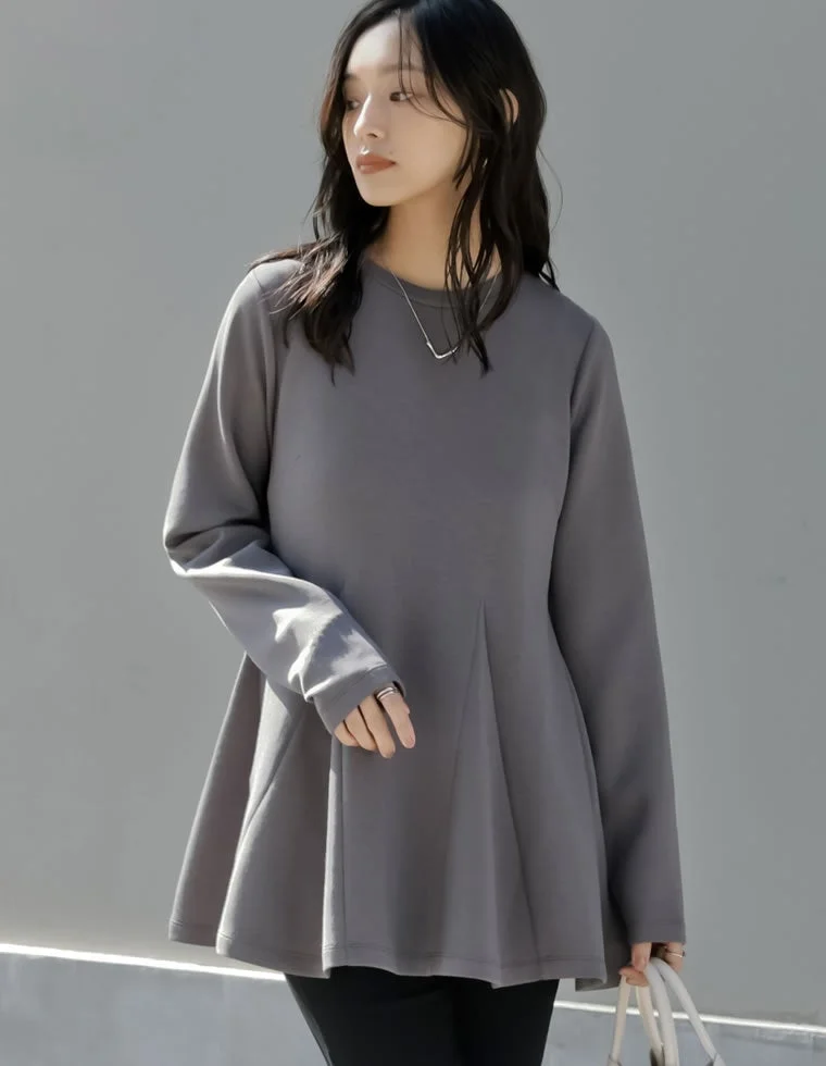 シンプルなグレーのペプラム長袖トップスと黒いパンツを着用した女性