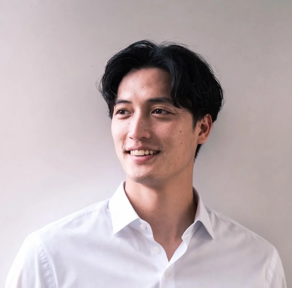 白いシャツを着たアジア人男性が、明るい笑顔で左方向を見ている上半身のポートレート写真