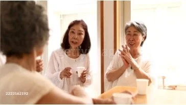 3人の高齢女性が屋内で集まり、カップを片手に談笑している様子