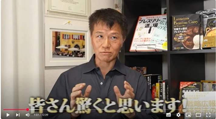 動画のスクリーンショットで、男性がカメラに向かって話しています。背景には書籍や商品が並んだ棚があり、画面下には「皆さん驚くと思います！」というテロップが表示されています。