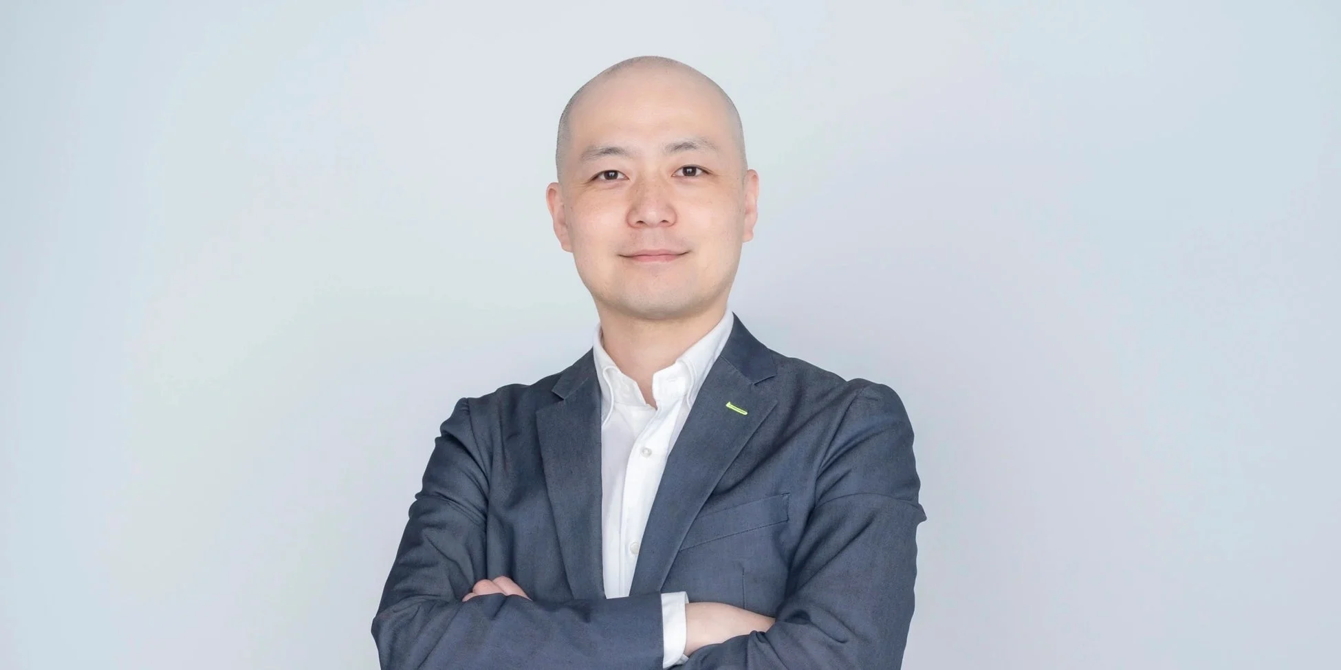 白い背景の前で、スーツを着用し腕を組んで穏やかに微笑む日本人男性のポートレートです。ビジネスシーンやプロフィール写真に適しています。