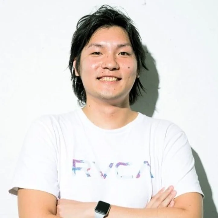 白いTシャツを着て腕を組み、カメラに向かって笑顔を見せる若いアジア人男性のポートレート。左手首にはスマートウォッチを着用しており、背景はシンプルな白です。