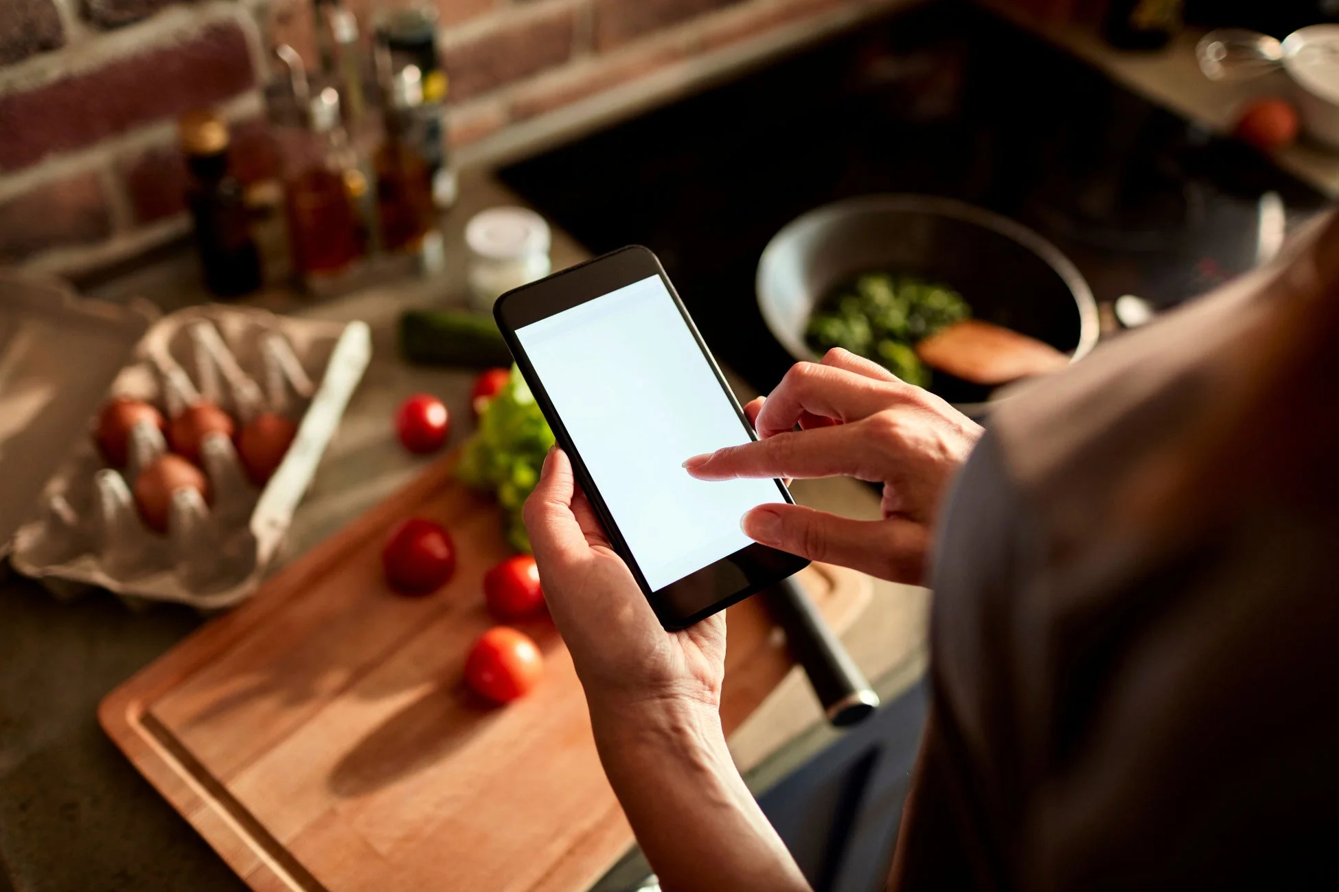 キッチンでスマートフォンを操作しながら料理をしている様子