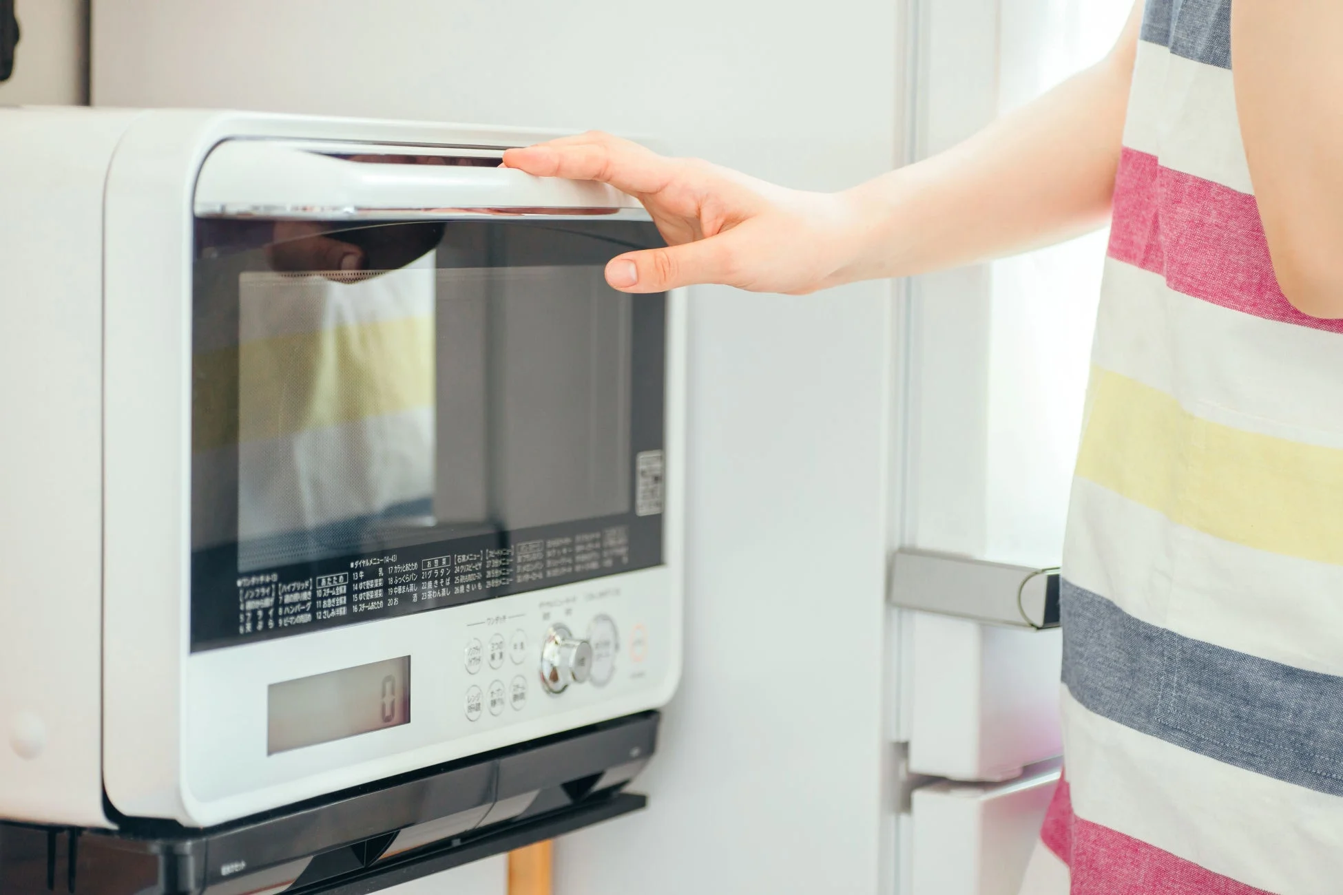 ストライプ柄の服を着た人物が、白い電子レンジのドアを開けようとしている